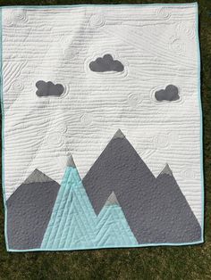 a quilted wall hanging with mountains and clouds in the sky on it's sides