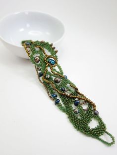 a green beaded bracelet sitting on top of a white bowl next to a spoon