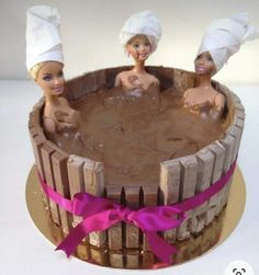 there are three barbie dolls in the bathtub on top of this cake, which is decorated with brown icing and pink ribbon