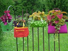 four purses are hanging on a fence with flowers in them and one is purple, the other is green