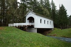 a white covered bridge over a stream in the middle of a green field with trees