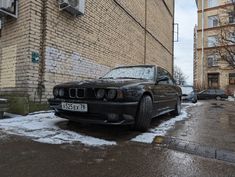 a black car parked in front of a brick building with snow on the ground next to it