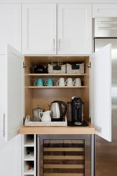 an open cabinet in the middle of a kitchen with coffee pots and tea kettles