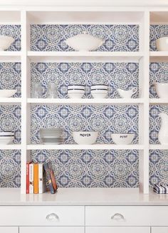 a kitchen with blue and white tiles on the wall, shelves filled with bowls and plates