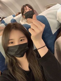 two women wearing face masks while sitting on an airplane with their hands in the air