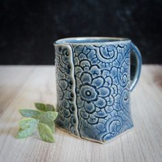 a blue and white mug sitting on top of a wooden table next to a green leaf