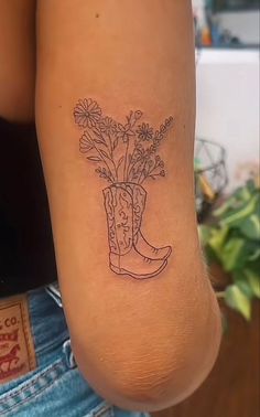 a woman with a tattoo on her arm has a cowboy boot and flowers in it