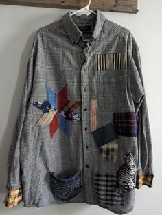 a shirt with patches and animals on it hanging from a wooden hanger next to a white wall