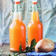 two glass bottles filled with sweet potato juice on top of a table next to potatoes