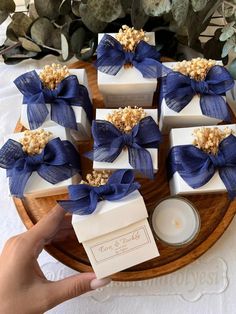 a person holding some white and blue wrapped presents on a wooden platter with candles