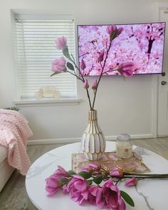 a vase with flowers on a table in front of a flat screen tv