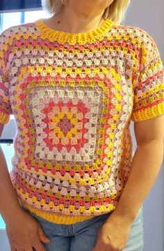 a woman standing in front of a window wearing a crocheted shirt and jeans