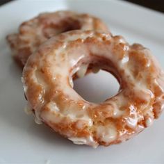 two glazed donuts sitting on top of a white plate next to eachother