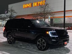 a black suv parked in front of a home depot store on a snowy street at night