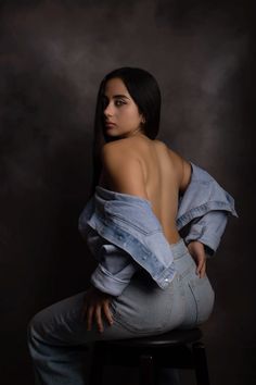 a woman sitting on top of a stool wearing blue jeans and a denim jacket over her shoulders