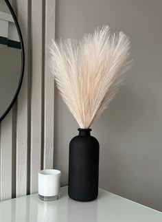 a black vase sitting on top of a white table next to a mirror and candle