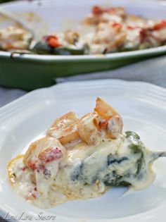 a white plate topped with lasagna covered in broccoli and cheese next to a green casserole dish