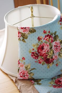 a lamp shade that is on top of a table with a flowered cloth covering it