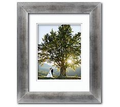 a framed photograph of a bride and groom standing under a tree with the sun behind them