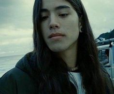 a man with long hair standing next to the ocean