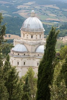 the dome of an old building is surrounded by trees and rolling hills in the distance