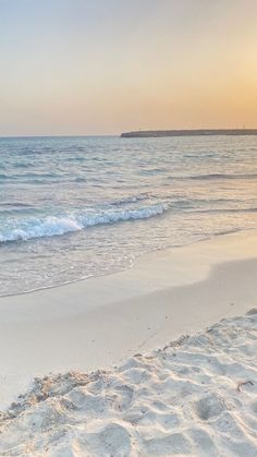 the surfboard is laying on the beach near the water's edge as the sun sets