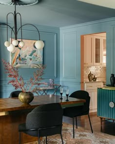 a dining room with blue walls and wooden table surrounded by black chairs, an art work on the wall