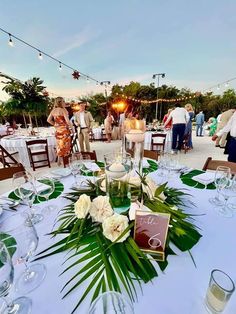 the table is set up for an event with white flowers and greenery on it