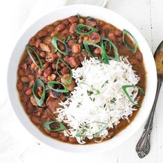 a white bowl filled with beans and rice next to a spoon on top of a table