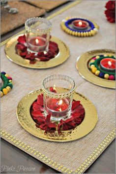 three candles are sitting on gold plates with red flowers in the center and other decorations around them