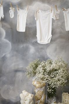 baby clothes hanging on the clothesline next to a vase with flowers and marshmallows