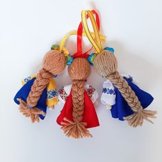 three braided dolls sitting next to each other on a white surface with red, yellow and blue ribbons