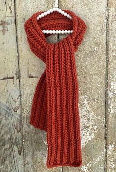 a red scarf hanging on a wooden wall with beads attached to the end of it