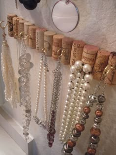 several wine corks are hanging on the wall with pearls and other jewelry attached to them