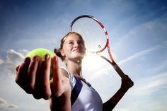 a woman holding a tennis racquet and ball in her hand with the sun shining behind her