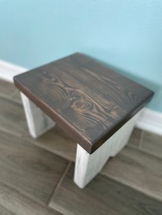 a small wooden stool sitting on top of a hard wood floor next to a blue wall