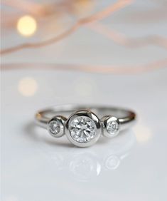 three stone diamond ring on white surface with blurry lights in the backround