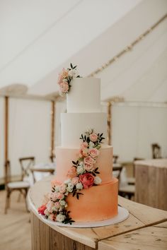 a wedding cake with pink and white flowers on the top is sitting on a table