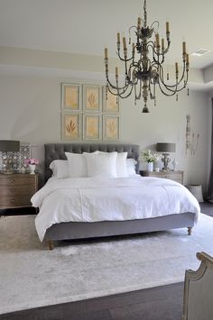 a large white bed sitting in a bedroom next to a chandelier