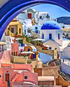 the view through an arched window shows colorful buildings and blue domes in oiai village, oiai