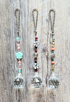 three necklaces with charms hanging from them on a wooden surface and one has a flower in the center