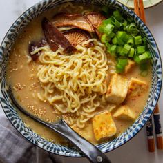 a bowl filled with noodles, tofu and green onions next to chopsticks