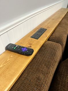 a remote control sitting on top of a wooden bench next to a wall with white paneling