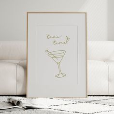 a framed photograph sitting on top of a white couch next to a painting with the words time to drink