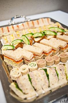 an assortment of sandwiches and cucumbers are arranged on a platter to be served