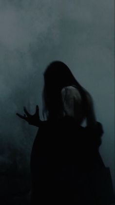 the silhouette of a woman with her hands out, in front of a foggy background