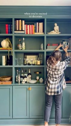 a woman standing in front of a bookshelf filled with lots of books and bottles