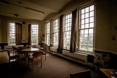 an empty room with tables and chairs in front of two large windows that have curtains on them