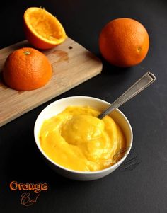 an orange is in a bowl next to two oranges on a cutting board with a spoon