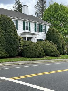 a white house with green shutters on the windows and bushes in front of it